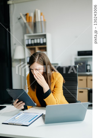 Woman who is tired and overthinking from working with tablet and laptop Woman who is tired and overthinking from working with tablet and laptop 130243006
