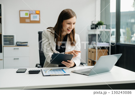 Confident business expert attractive smiling young woman typing laptop and holding digital tablet Confident business expert attractive smiling young woman typing laptop and holding digital tablet 130243086
