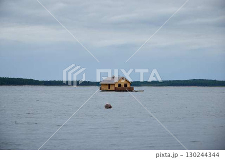 A Yellow Cabin rests on calm water under a cloudy sky, evoking peace and serenity A Yellow Cabin rests on calm water under a cloudy sky, evoking peace and serenity 130244344