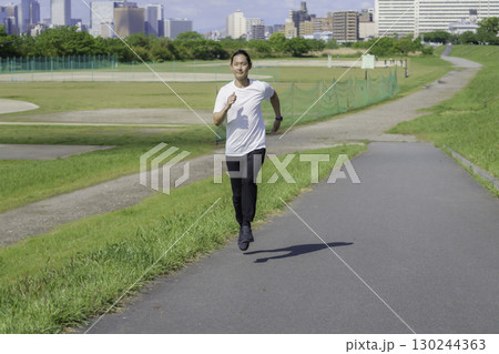 多摩川の土手をランニングしながらスマートウォッチをチェックする若い男性 130244363
