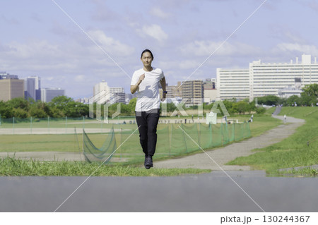 多摩川の土手をランニングする若い男性 130244367