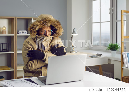 Young african american man working in the cold at home on his laptop computer trying to keep warm. Young african american man working in the cold at home on his laptop computer trying to keep warm. 130244732