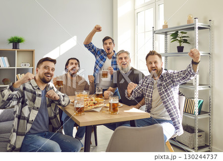Group of excited friends watching football match on tv at home with beer and snacks. 130244737