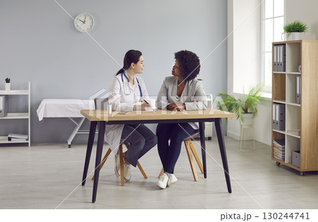 Woman doctor and her patient sitting at table and talking about medical prescription Woman doctor and her patient sitting at table and talking about medical prescription 130244741