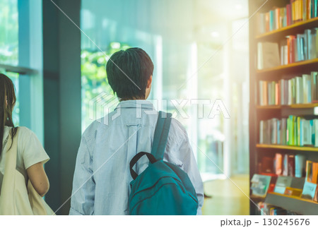 本棚が並ぶ図書館を歩く学生男女 本棚が並ぶ図書館を歩く学生男女 130245676