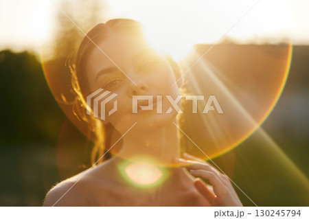 Young woman enjoying a sunset, with soft light illuminating her face and a dreamy expression, ideal for serene lifestyle concepts and summer themes 130245794