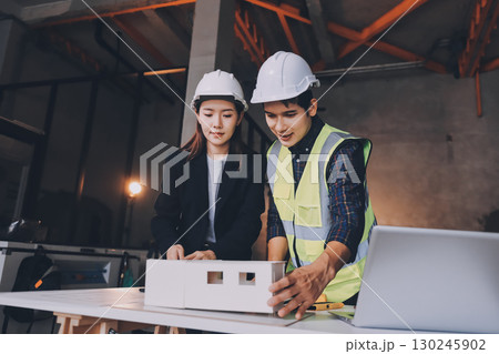 Construction manager and engineer dressed in orange work vests and hard helmets explore construction documentation on the building site near the steel frames 130245902