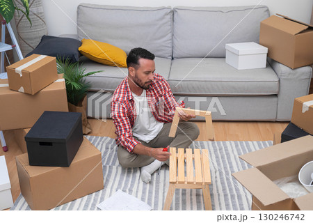 DIY Relocation Project: Amidst moving boxes, a young man engages in DIY shelf assembly, personalizing his new dwelling after relocating. DIY Relocation Project: Amidst moving boxes, a young man engages in DIY shelf assembly, personalizing his new dwelling after relocating. 130246742