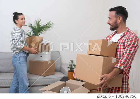 New Living Space: A satisfied young couple stands in their new home's living room, surrounded by a heap of cardboard boxes from their international relocation, making their space their own New Living Space: A satisfied young couple stands in their new home's living room, surrounded by a heap of cardboard boxes from their international relocation, making their space their own 130246750