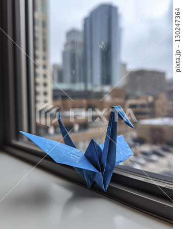 Blue origami crane sits perched on windowsill, gazing thoughtfully at cityscape outside. city rises with sense of hope and wonder 130247364