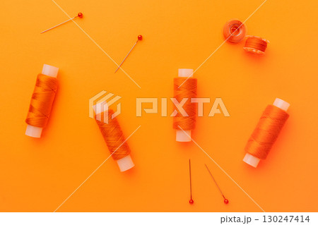 Orange sewing threads and pins on bright background 130247414