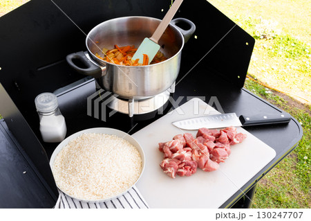 Outdoor cooking setup with pot and ingredients for rice and meat dish Outdoor cooking setup with pot and ingredients for rice and meat dish 130247707