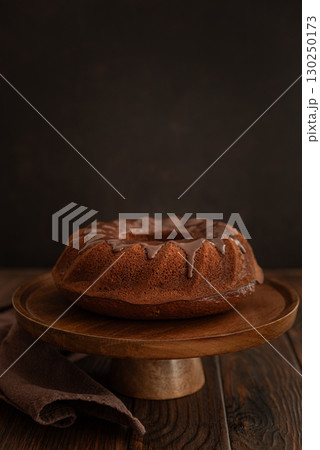 Chocolate cake with chocolate icing on dark wooden table. Low key. Front view Chocolate cake with chocolate icing on dark wooden table. Low key. Front view 130250173