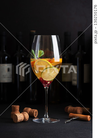 Sangria with citrus fruits and mint, corks and a corkscrew on a dark table with wine bottles. 130250176