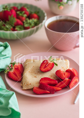 Crepes with chocolate spread and fresh strawberries, served with tea on pink background 130250188