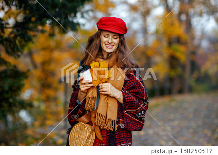 smiling modern woman in red hat with autumn leafs walking 130250317