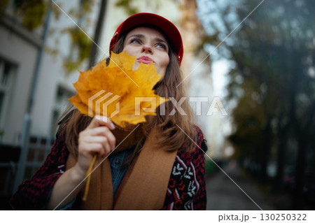 cheerful trendy woman with autumn leafs and scarf in city 130250322