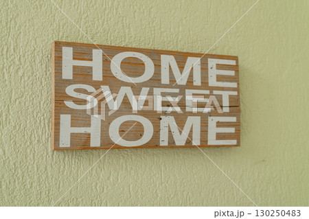 Wooden wall sign with bold white letters displaying the phrase Home Sweet Home evokes warmth and comfort. Mounted on a textured surface, it enhances homely ambiance Wooden wall sign with bold white letters displaying the phrase Home Sweet Home evokes warmth and comfort. Mounted on a textured surface, it enhances homely ambiance 130250483