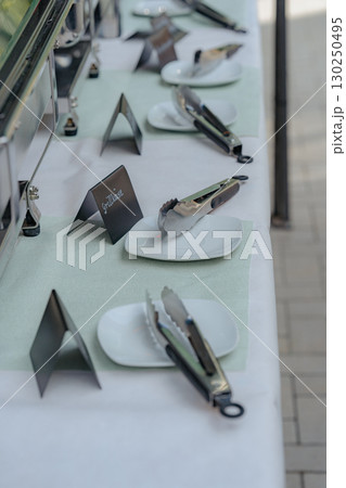 Close-up view of a buffet table prepared for guests, featuring white square plates, serving tongs, and black food labels. Elegant catering setup for events, weddings, or parties. Ideal for Close-up view of a buffet table prepared for guests, featuring white square plates, serving tongs, and black food labels. Elegant catering setup for events, weddings, or parties. Ideal for 130250495