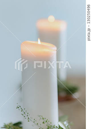 White candles softly glow, surrounded by delicate greenery. The serene and calming atmosphere enhances the focus on warmth and tranquility, perfect for peaceful settings or meditative moments White candles softly glow, surrounded by delicate greenery. The serene and calming atmosphere enhances the focus on warmth and tranquility, perfect for peaceful settings or meditative moments 130250496