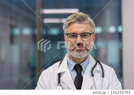 Experienced male physician wearing glasses and stethoscope standing professionally in a modern healthcare facility. Ideal for themes of healthcare, medical expertise 130250791