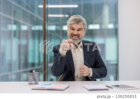 Businessman in formal attire expressing anger and frustration while pointing in an office setting. Businessman in formal attire expressing anger and frustration while pointing in an office setting. 130250833