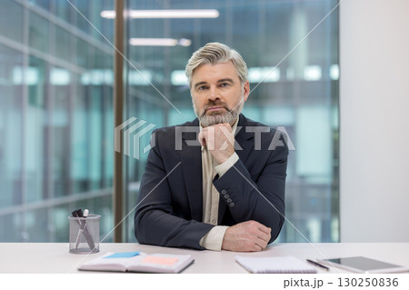 Professional businessman seated at a desk in a contemporary office environment, displaying a composed and introspective demeanor. 130250836