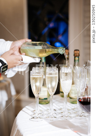 Waiter pouring sparkling wine into glasses at elegant celebration event table Waiter pouring sparkling wine into glasses at elegant celebration event table 130250945