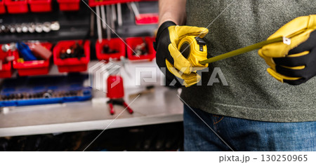 Man In Protective Gloves Holds A Measuring Tape At The Workbench Man In Protective Gloves Holds A Measuring Tape At The Workbench 130250965
