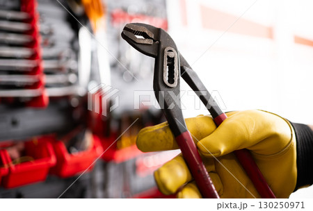 Auto Mechanic With Pliers Against Tool Wall In Service Center 130250971