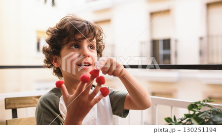 Smiling child playing with raspberries on balcony: healthy eating habits 130251194