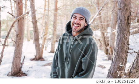 Young man smiling in snowy forest wearing hoodie and beanie 130251224