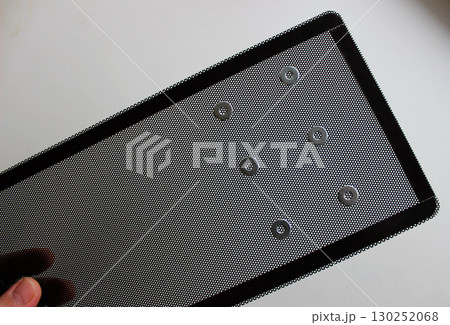 Man fingers hold plastic grill for dust protection with iron washers on a perforated surface Man fingers hold plastic grill for dust protection with iron washers on a perforated surface 130252068