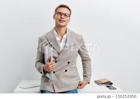 Professional cheerful young man in gray blazer holding documents smiling confidently in modern office interior. Business casual style male executive working, corporate lifestyle concept. Professional cheerful young man in gray blazer holding documents smiling confidently in modern office interior. Business casual style male executive working, corporate lifestyle concept. 130252950