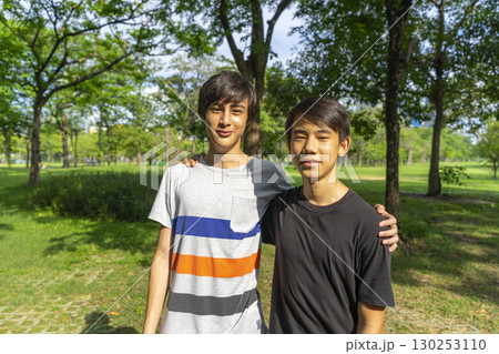 Two joyful teenage boys looking at the camera in the summer park against the blue sky. 130253110