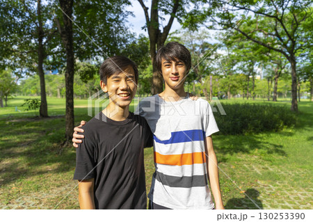 Two joyful teenage boys looking at the camera in the summer park against the blue sky. 130253390