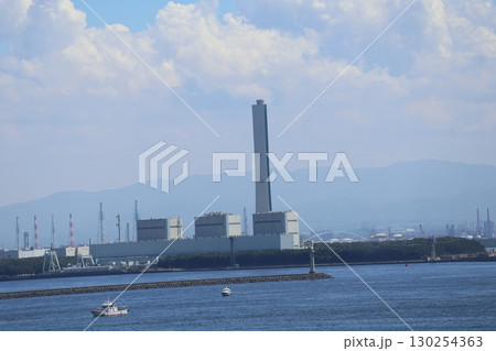雲と霞む青空と山並みと海岸沿いの工場と青い海面の海と船舶のある風景 130254363