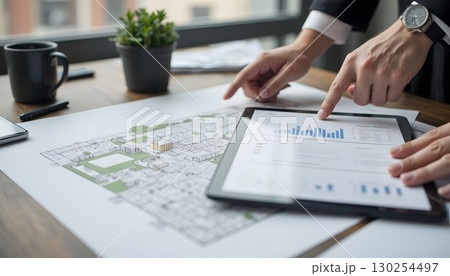 Business professionals analyzing architectural plans and data on a digital tablet 130254497