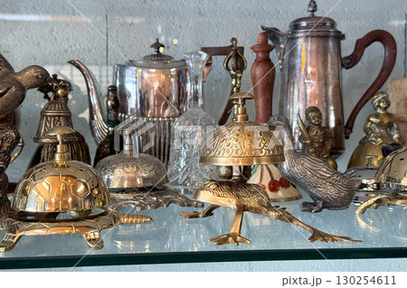 A detailed shelf of vintage brass bells, teapots, and ornamental objects shaped like animals in a flea market shop. Flea market style, one-of-a-kind style, identity in fashion, retro self-expression 130254611