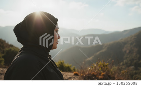Woman in Black Hijab Facing Mountains and Hills Under Bright Sunlight with Blue Sky Background 130255008