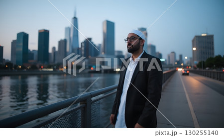Man in Suit by River with City Skyline at Dusk, Urban Landscape with Modern Architecture 130255140