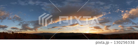 Stunning sunset fills sky with rich hues of blue and orange. Dramatic clouds with hints of pink and gold spread across sky. Silhouettes of hills in foreground add depth to breathtaking evening scene. 130256338