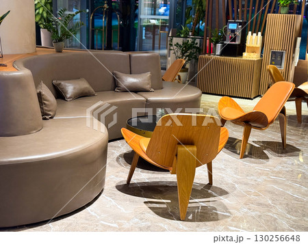 Modern lounge with curved sofa and wooden chairs. Relaxation, comfort and hospitality design in stylish hotel interior. 130256648