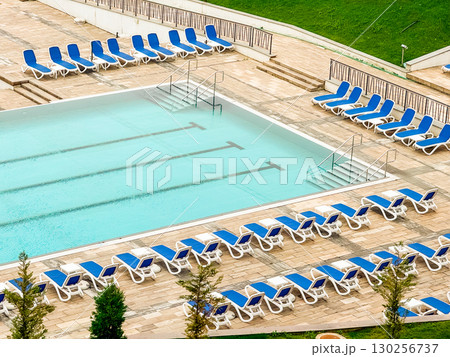 Outdoor swimming pool with blue loungers arranged around the deck in a resort setting. Tourism, leisure, and recreation symbolizing vacation lifestyle, wellness, and modern hospitality. 130256737