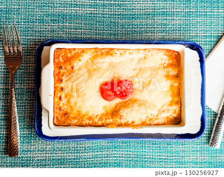 Baked lasagna with cheese crust and sliced tomato topping served on a table setting. Cuisine, dining, and homemade comfort food symbolizing tradition, taste, and culinary lifestyle. 130256927