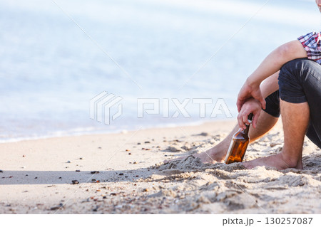 Man depressed with wine bottle sitting on beach outdoor 130257087