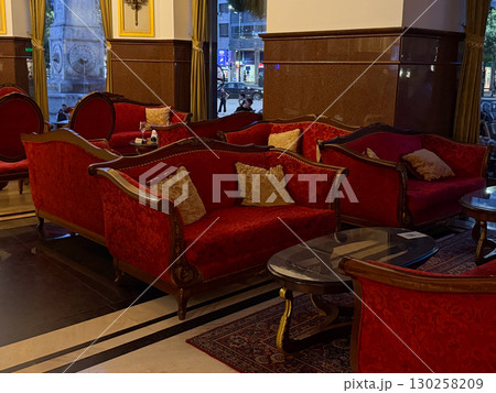 Multiple red vintage sofas in hotel lounge interior. Classic decor with glass tables, ornate details and evening atmosphere. Multiple red vintage sofas in hotel lounge interior. Classic decor with glass tables, ornate details and evening atmosphere. 130258209