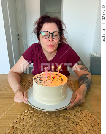 Woman blowing out candles on birthday cake. Celebration, tradition and joyful wish-making moment at festive party. Woman blowing out candles on birthday cake. Celebration, tradition and joyful wish-making moment at festive party. 130258212