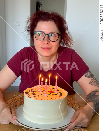 Happy woman holding birthday cake with lit candles. Celebration, joy and festive atmosphere at home gathering. 130258213