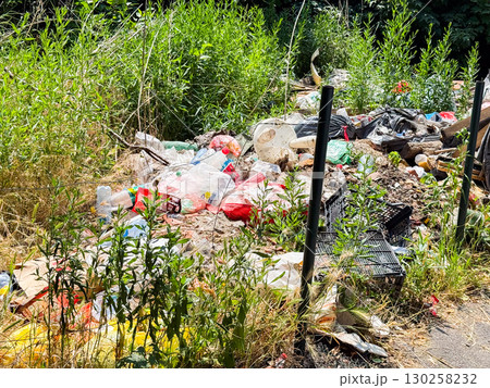 Pile of garbage and plastic waste among green grass. Pollution, environmental damage, and ecological issues in urban surroundings. 130258232
